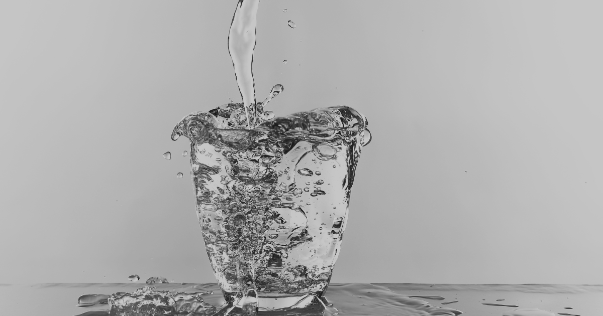 Water is being poured into a glass, causing it to overflow onto a reflective surface.